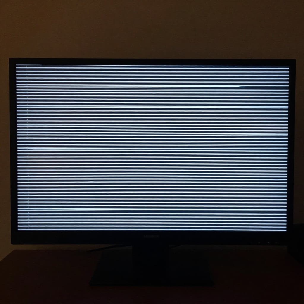 En computerskærm placeret på et kontorbord viser vandrette striber og visuelle forstyrrelser på displayet.
